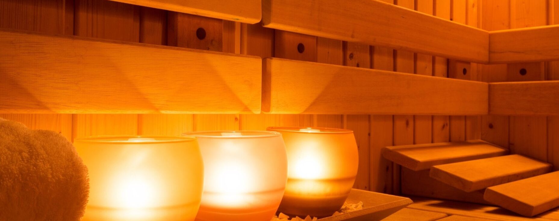 A sauna with wooden benches and three lit candles.