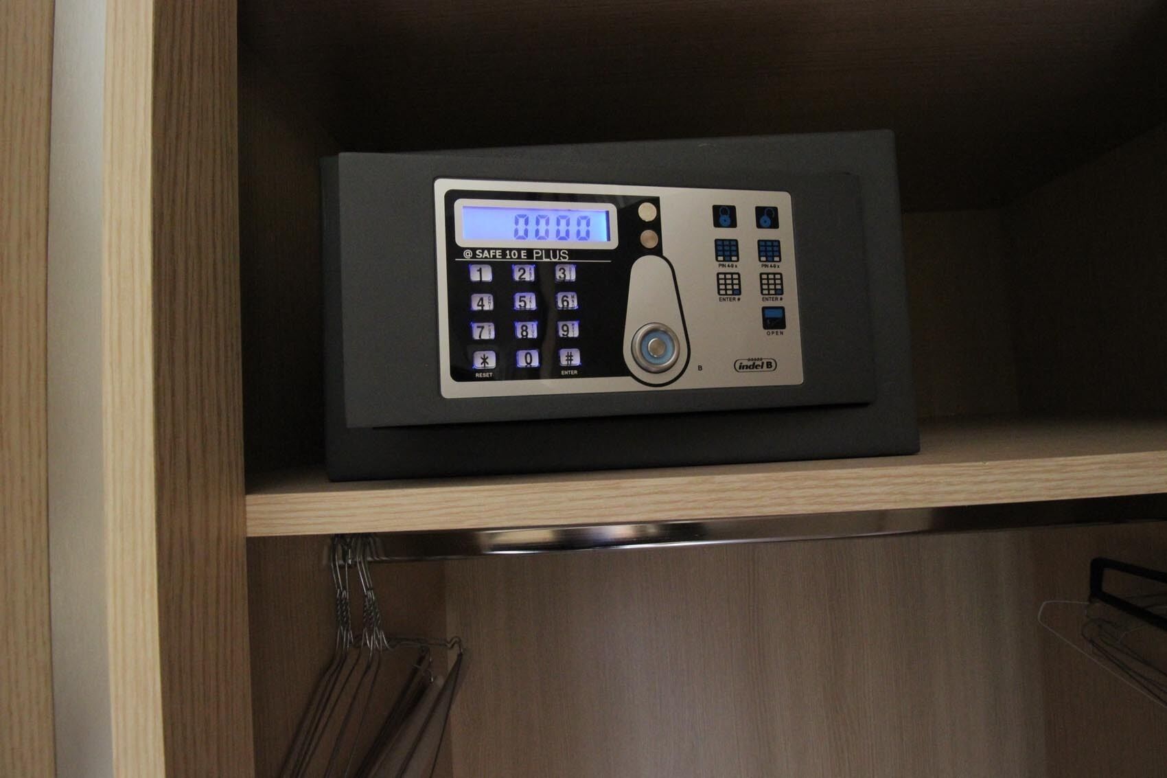 A digital safe with a keypad and a display screen on a wooden shelf.