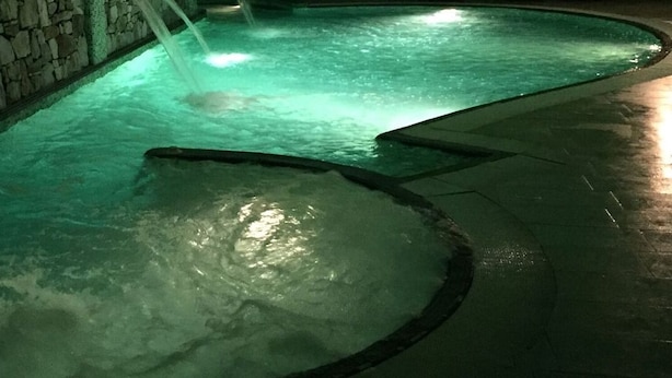 A swimming pool with a stone wall and a water feature.