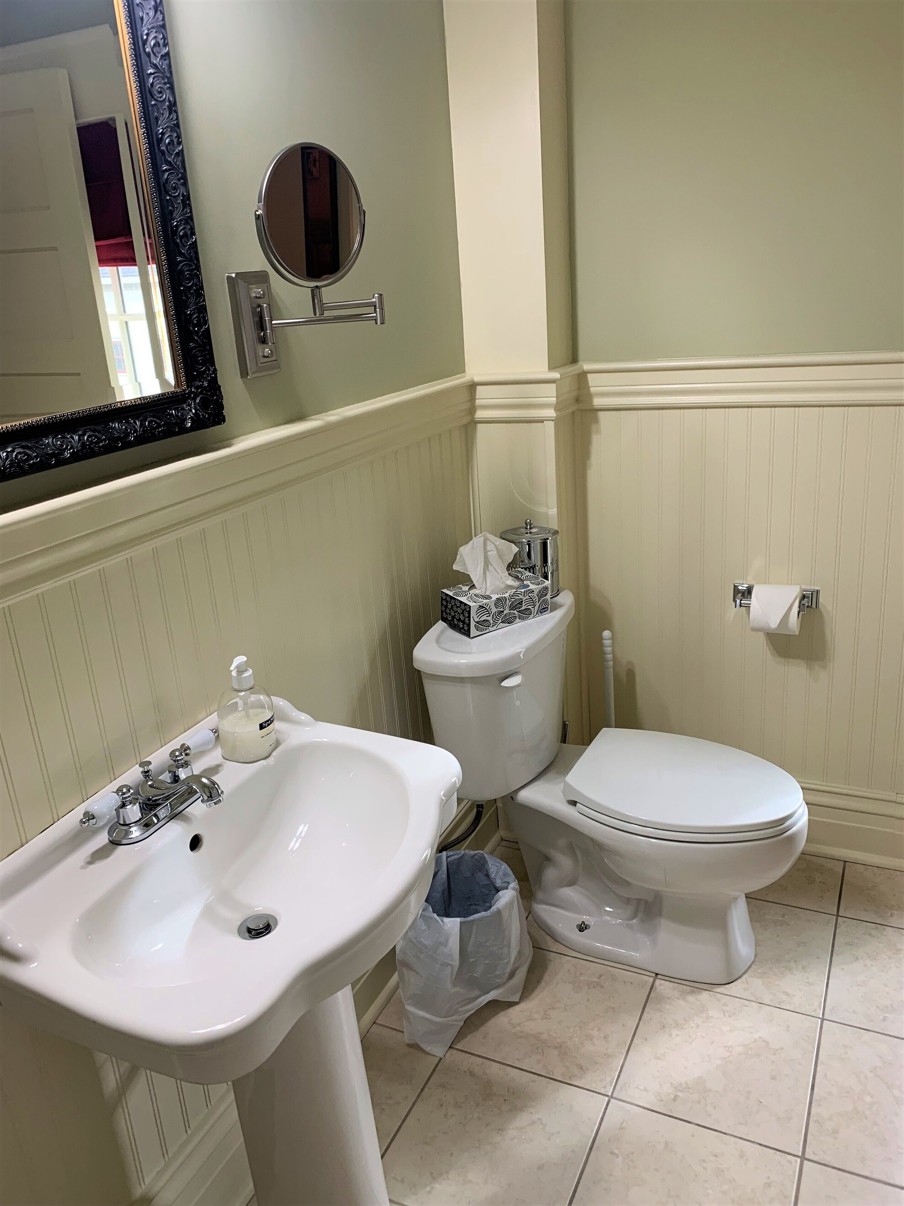 A bathroom with a white sink, a toilet, and a bidet. There is a mirror above the sink, and a toilet paper holder is visible on the wall.
