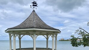 A gazebo with a weather vane, surrounded by a grassy area and a body of water in the background. - The Red Coat Bed & Breakfast (Niagara-on-the-Lake)