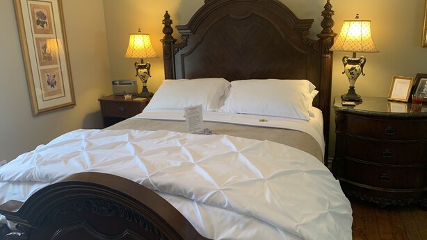 Una cama bien hecha con tablero de madera, dos mesitas de noche con lámparas y cuadros en la pared.