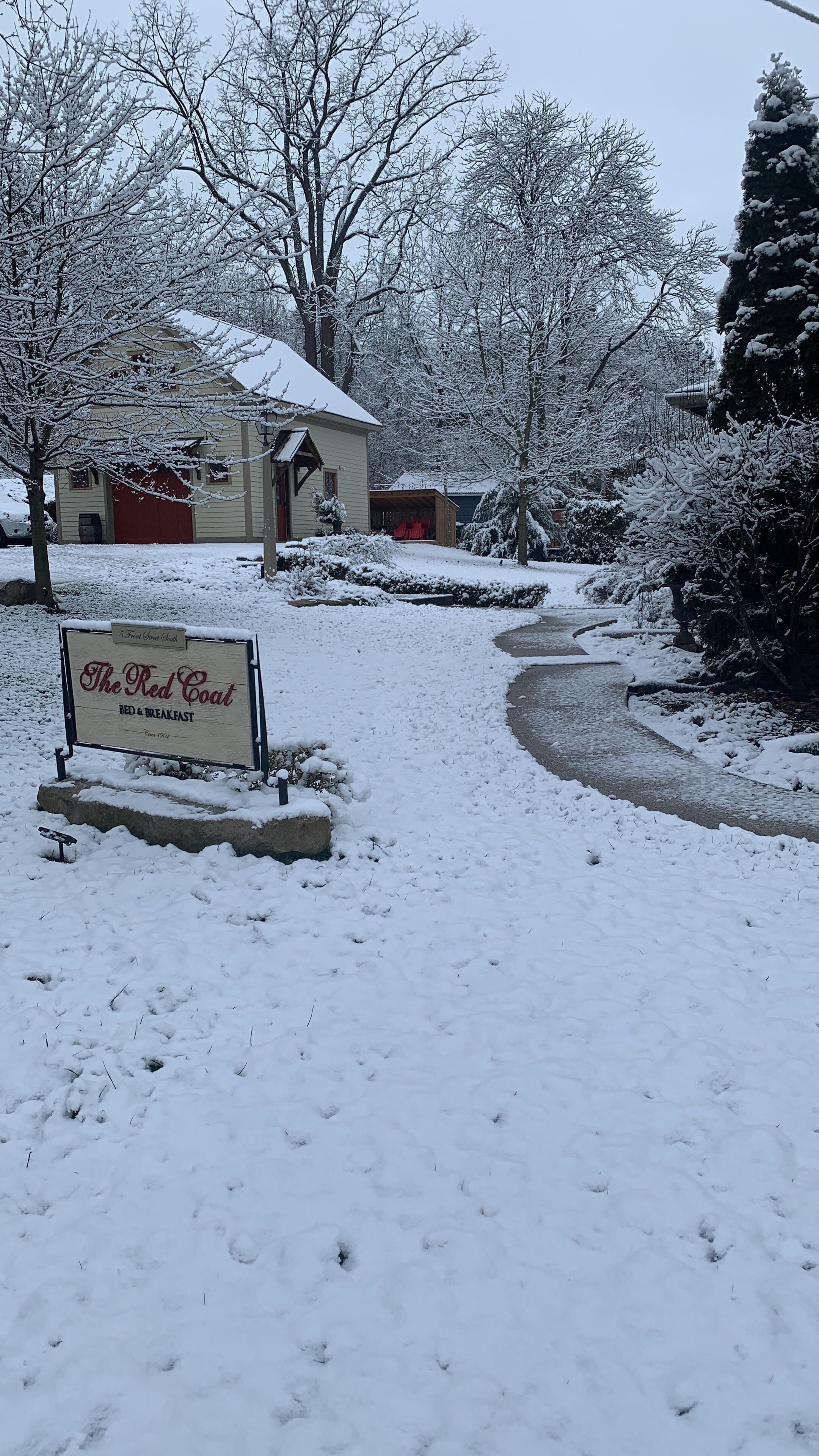 Un paysage enneigé avec un panneau indiquant « The Red Coat Bed & Breakfast » et un chemin menant à un bâtiment.