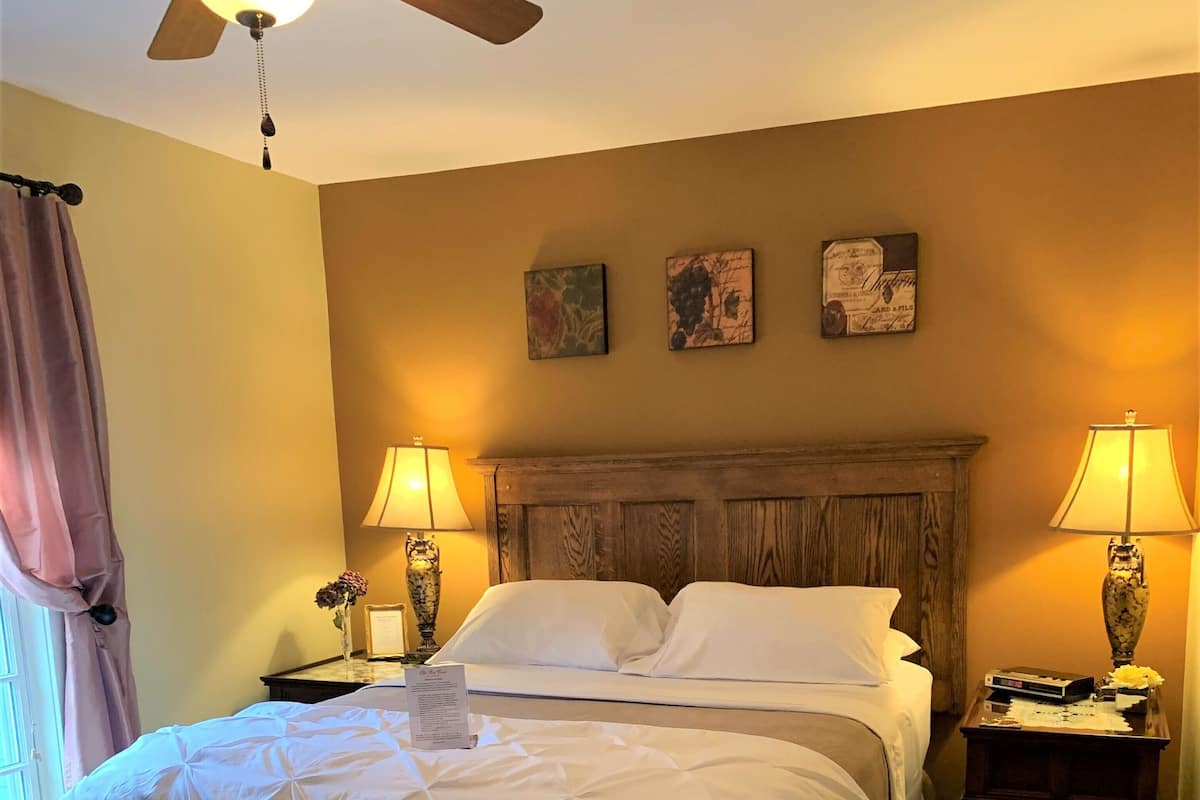A hotel room with a large bed, two bedside lamps, a ceiling fan, and a window with curtains.