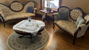 A room with two upholstered armchairs, a round coffee table with a lace tablecloth, and a small table with a lamp and a potted plant. - The Red Coat Bed & Breakfast (Niagara-on-the-Lake)