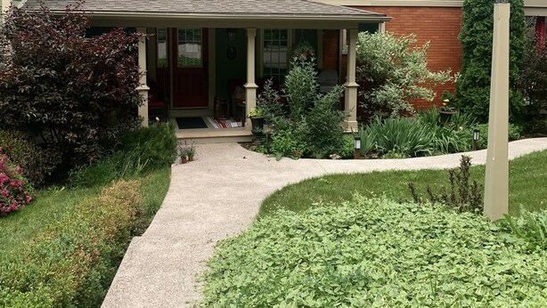 A two-story house with a green exterior, a covered porch, and a brick chimney. - The Red Coat Bed & Breakfast (Niagara-on-the-Lake)
