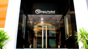The entrance to Tempo Hotel with a glass facade, steps leading up to the door, and potted plants on either side.