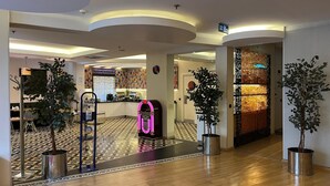 A hotel lobby with a check-in counter, a neon sign, and potted plants.