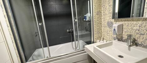 A bathroom with a glass-enclosed shower, a white sink, and a mirror.