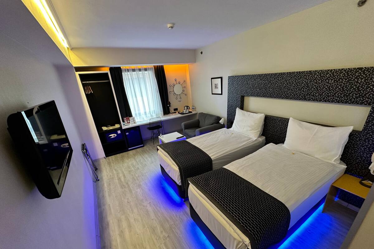 Een hotelkamer met twee bedden, een bureau, een stoel, een televisie en een raam met gordijnen.