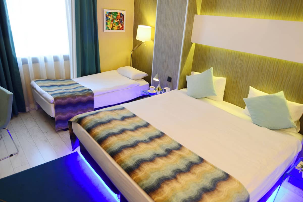 A hotel room with two single beds, a desk, a chair, a lamp, and a painting on the wall.