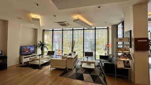 Ein modernes Hotelzimmer mit großem Fenster, Flachbildfernseher, einer Couch, einem Couchtisch und einem kleinen Schreibtisch.