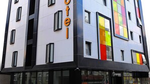 Ein modernes Hotelgebäude mit einem gut sichtbaren 'Tempo Hotel'-Schild, großen Fenstern und einer markanten Fassade mit farbigen Paneelen.