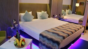 Ein Hotelzimmer mit einem großen Bett, einem Nachttisch mit Obstkorb, einer Lampe und einem Spiegel.