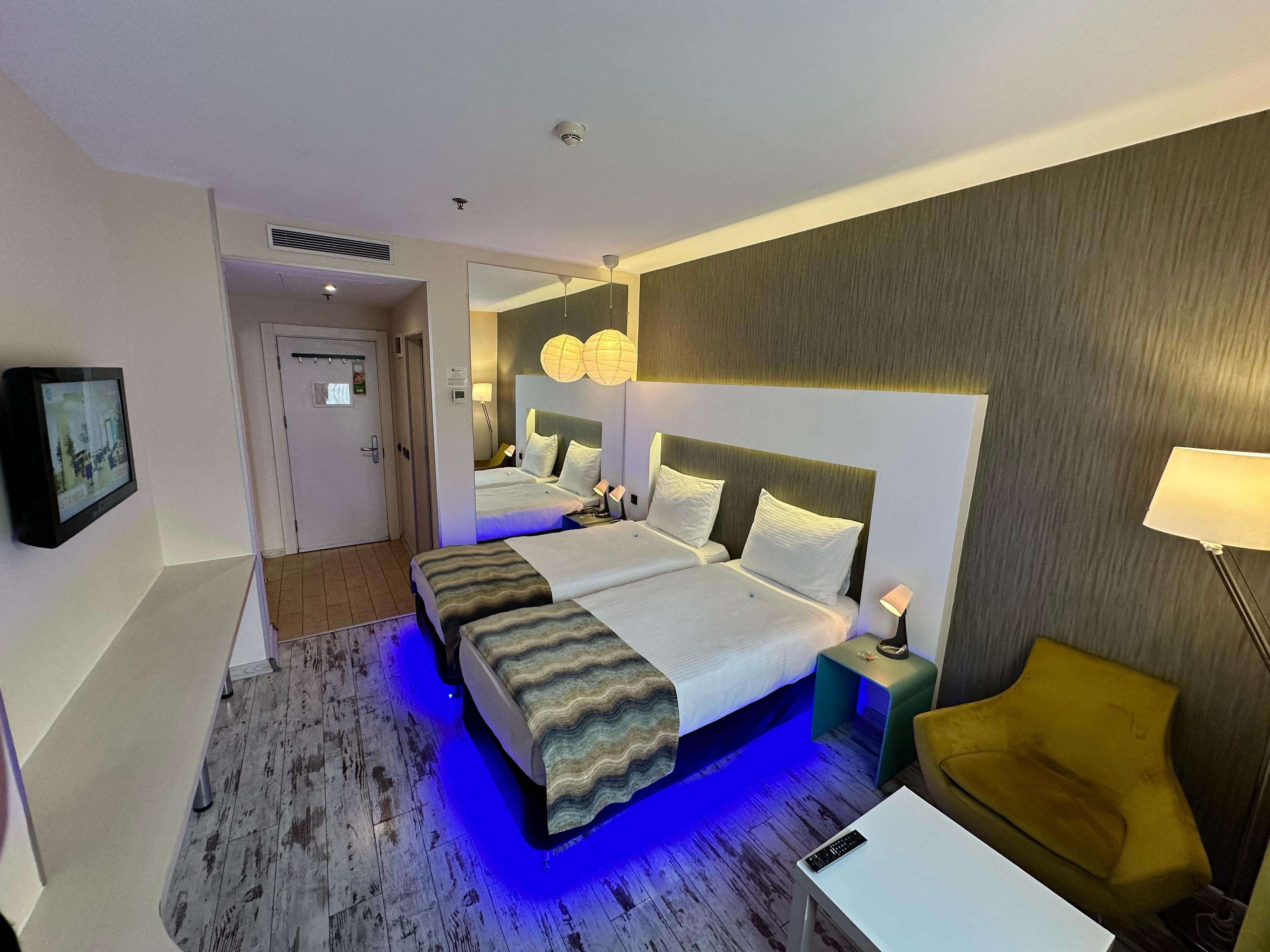 A hotel room with two beds, a desk, a chair, and a TV.