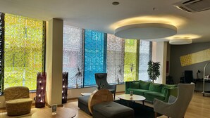 Un área de descanso moderna con un sofá verde, sillones, una mesa de centro y paneles decorativos en las ventanas.