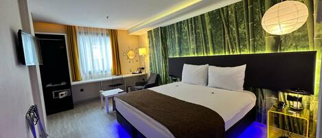 A modern hotel room with a large bed, a desk with a chair, a TV, and a wall with a bamboo forest mural.