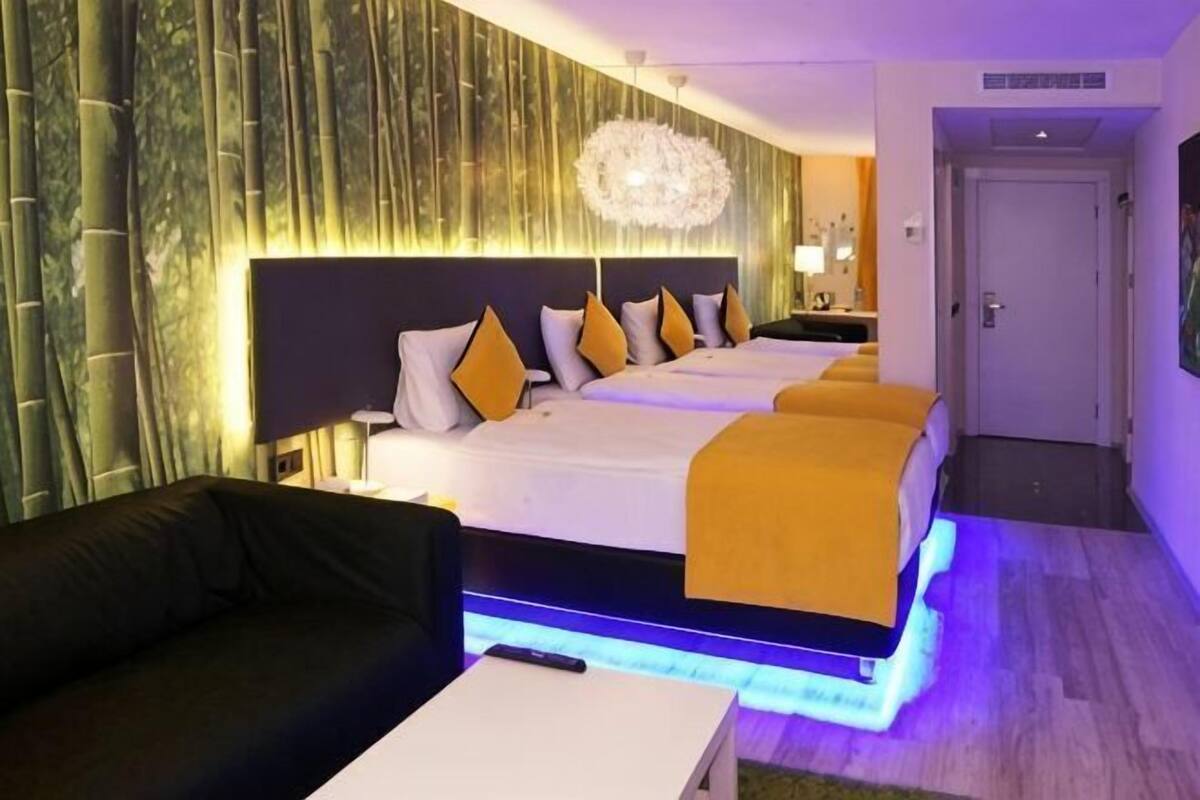 Une chambre d’hôtel avec un grand lit, un canapé, une table de chevet et un mur orné de lignes verticales.