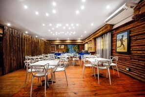 A dining area with round tables and white chairs, wooden walls, and ceiling lights.