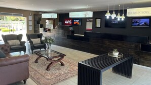 A reception area with a reception desk, AVIS and Budget signs, a reception sign, and a television screen. - Musina Hotel (Musina)