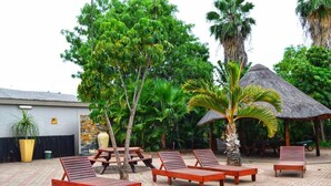 A poolside area with lounge chairs, a thatched-roof structure, and lush tropical vegetation. - Musina Hotel (Musina)
