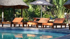 A poolside area with wooden lounge chairs and a thatched umbrella. - Musina Hotel (Musina)