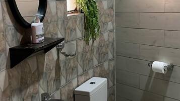 Une salle de bain avec un lavabo blanc, des toilettes, un miroir et une petite fenêtre avec une plante.