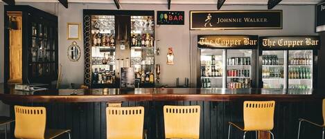 Un bar con mostrador de madera, cuatro sillas amarillas y estantes llenos de botellas.