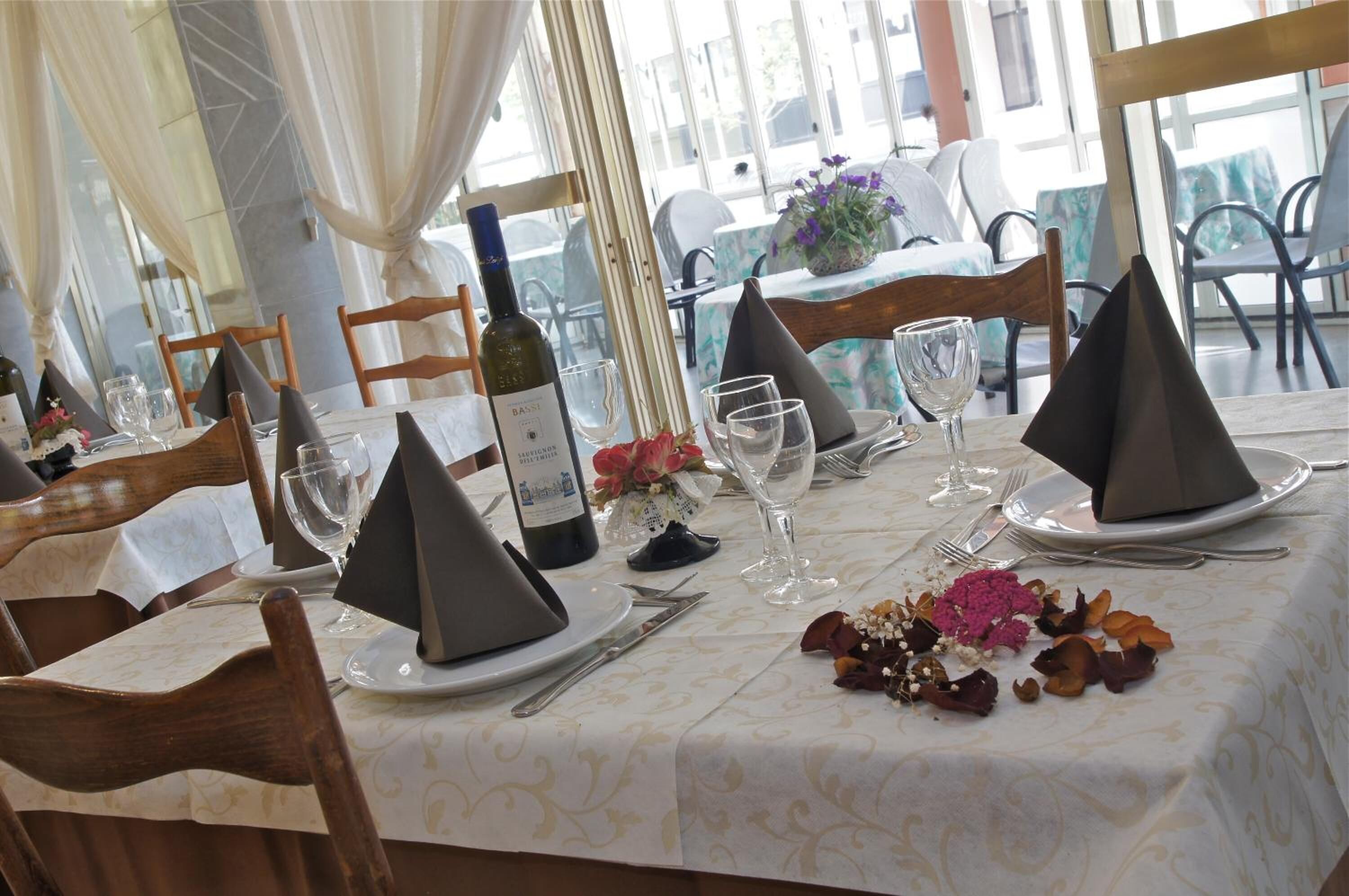 A dining table set with dark napkins, wine glasses, and a bottle of wine.