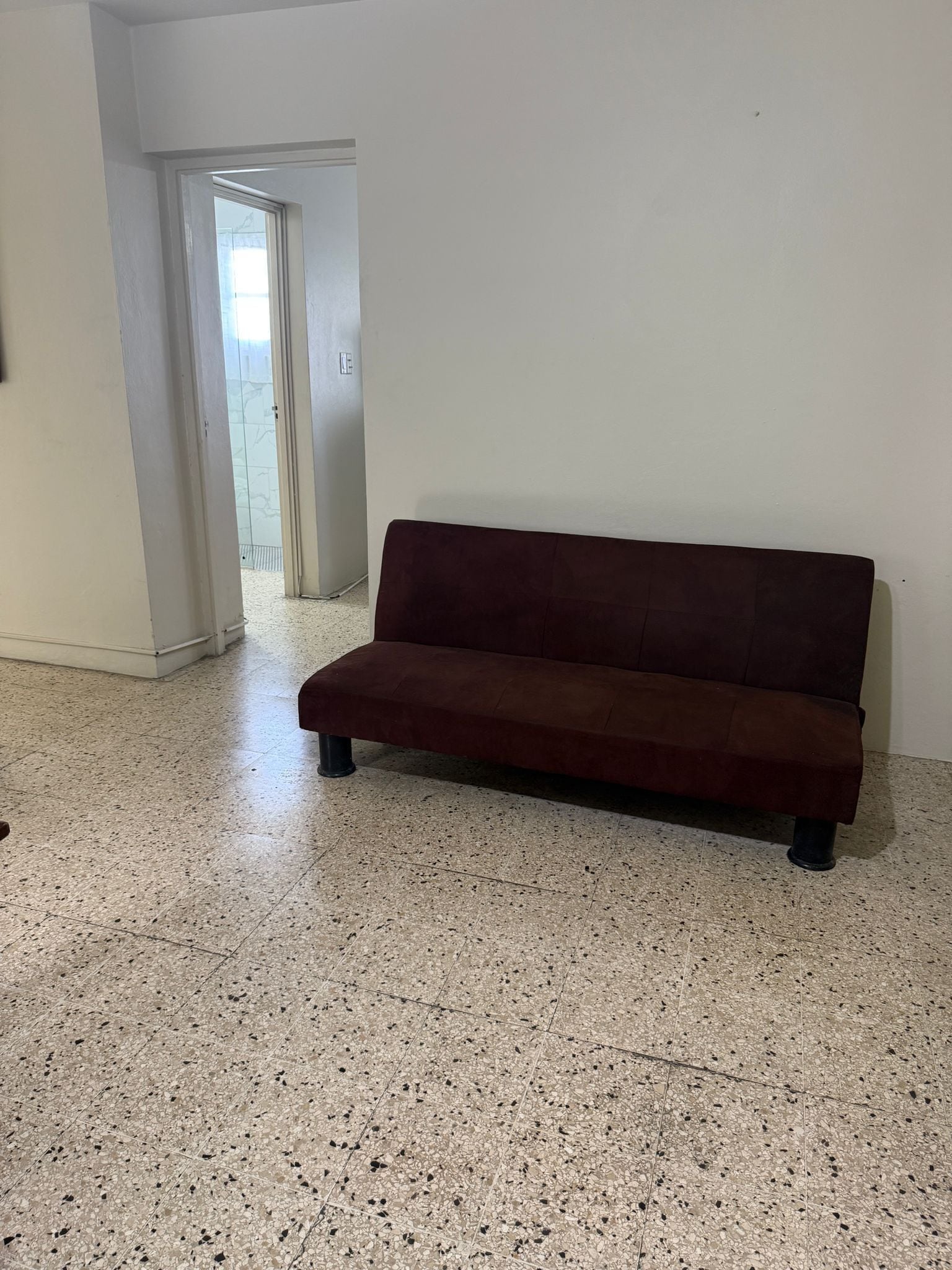 A room with a dark brown sofa, white walls, and a speckled floor.