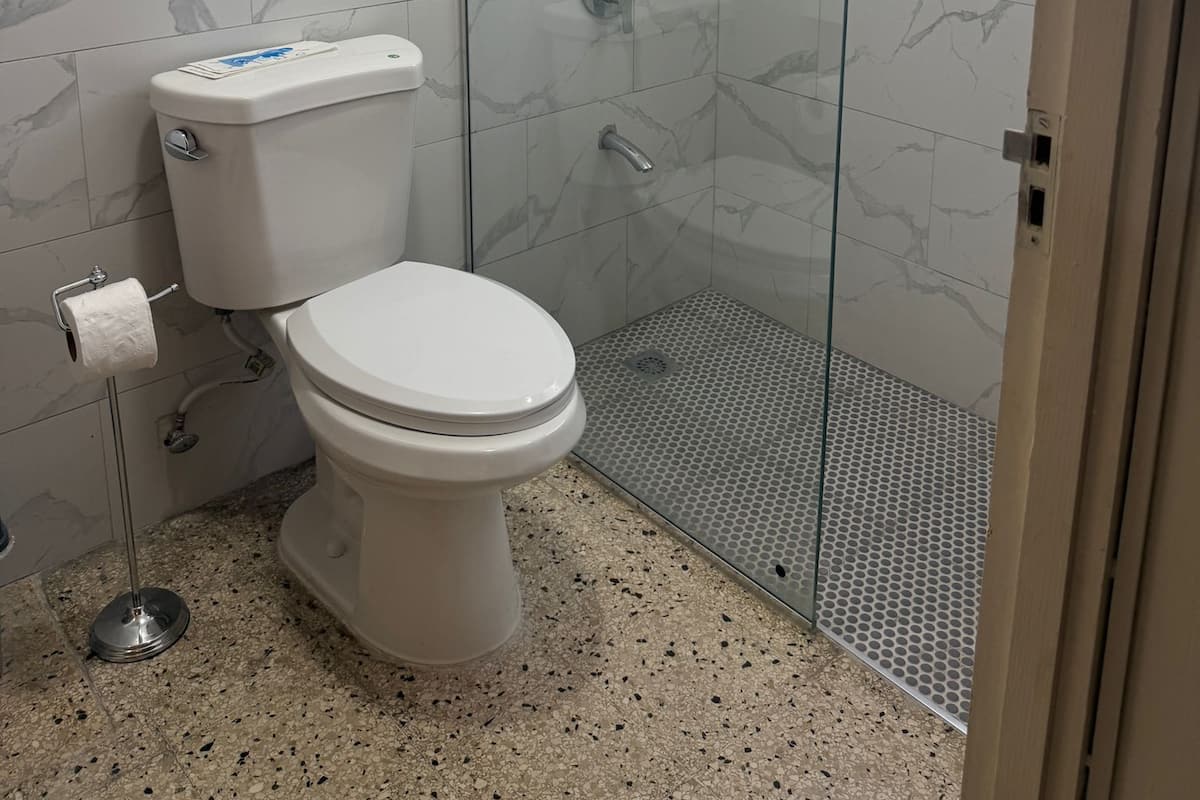 Un baño con inodoro, ducha con puerta de cristal y ventana con cortina.