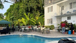 A poolside area with tables and chairs, a buffet setup, and a building with balconies. - Palm View Guesthouse and Conference Centre (Montego Bay)