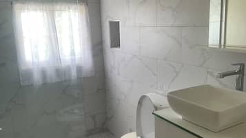 Un baño con cabina de ducha de vidrio, inodoro y lavamanos con espejo.