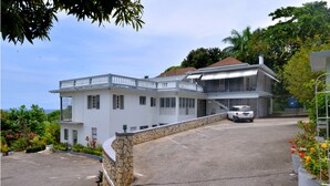 A two-story building with a white exterior, a stone retaining wall, and a parking area. - Palm View Guesthouse and Conference Centre (Montego Bay)