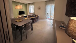 Una sala moderna con comedor, sofá, televisor y un gran ventanal con cortinas.