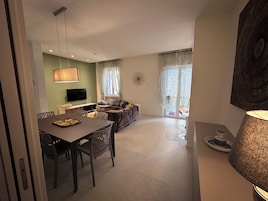 Un soggiorno moderno con zona pranzo, divano, televisore e un'ampia finestra con tende.