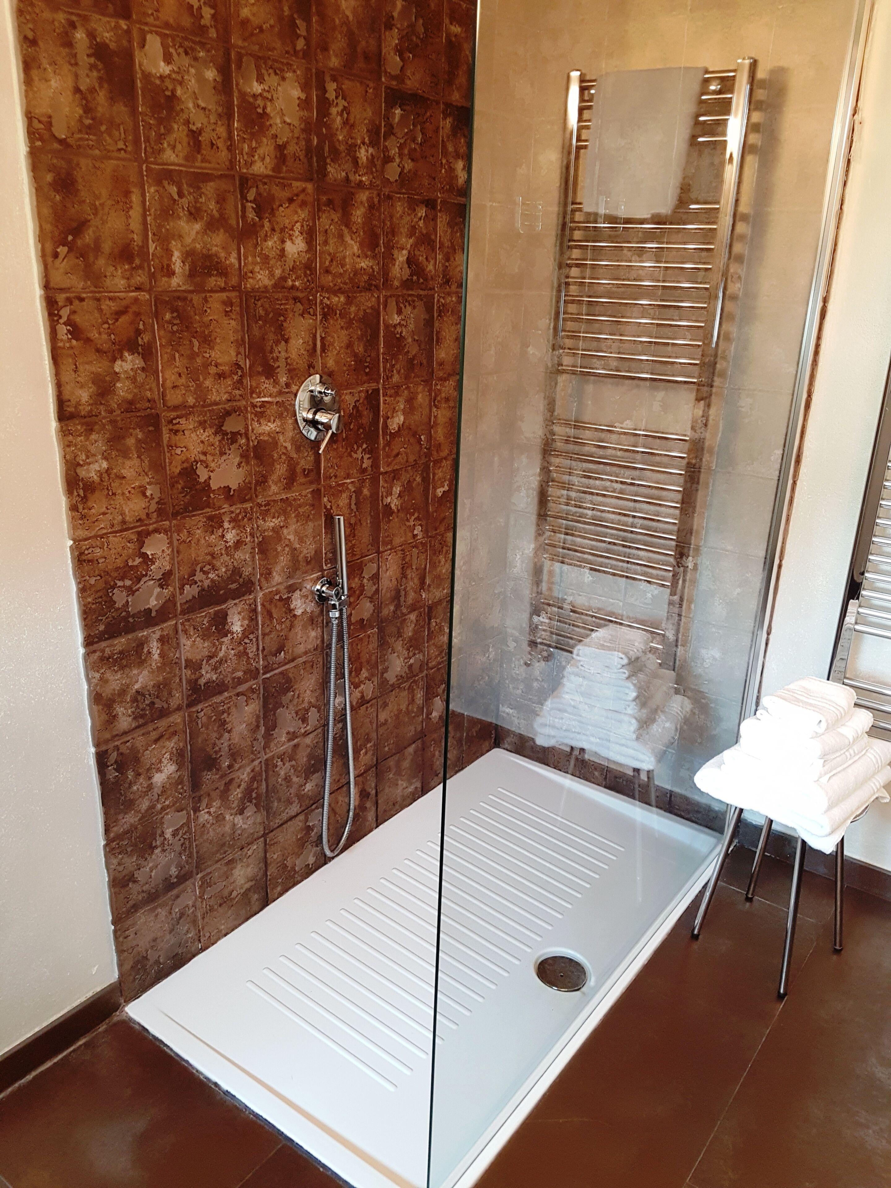 Ein modernes Duschbad mit Glastür, weißer Sitzgelegenheit und Handtuchhalter.