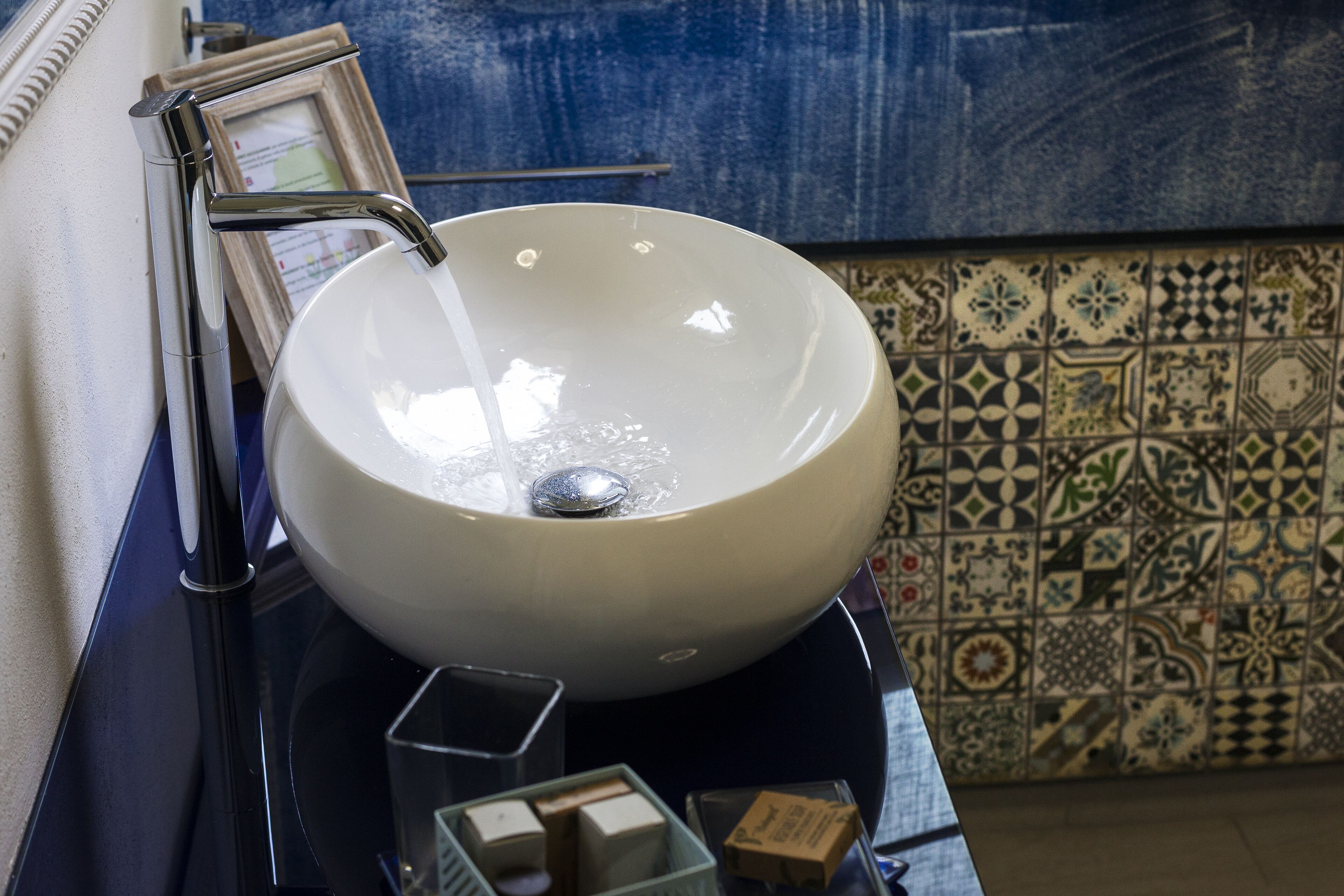 A white ceramic sink with a chrome faucet, a framed picture, and a small soap dispenser on a dark countertop.