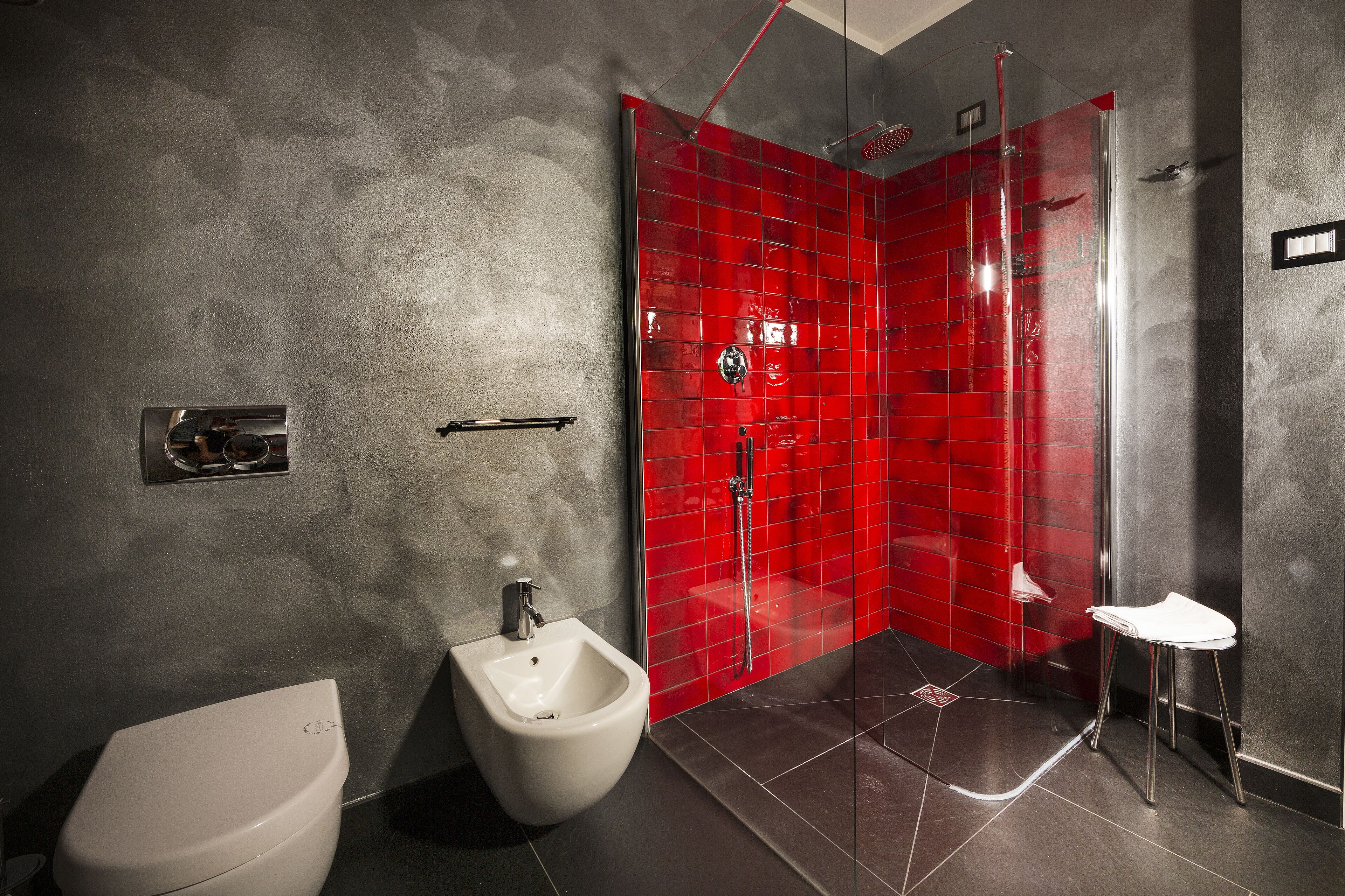 Un baño moderno con un bidé, una cabina de ducha con mampara de vidrio y un lavamanos pequeño.