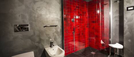 Un baño moderno con un bidé, una cabina de ducha con mampara de vidrio y un lavamanos pequeño.