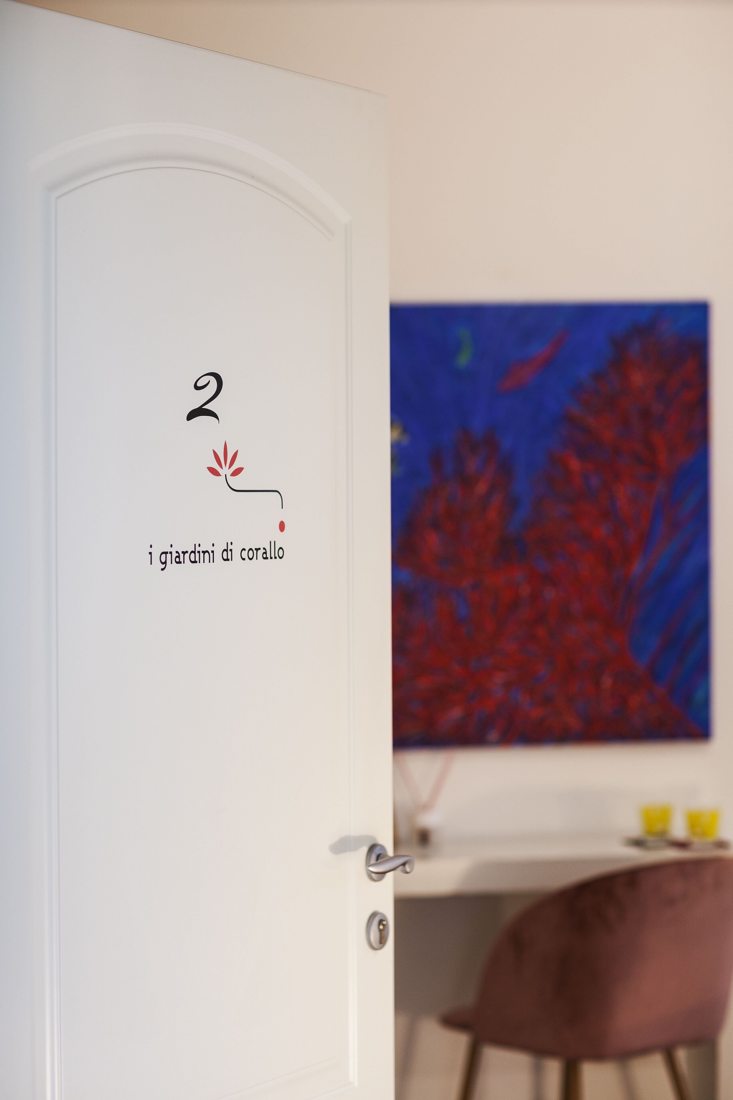 Eine Tür mit der Nummer 2 und einem Logo, ein Gemälde von rotem Korallen und ein Essbereich mit einem Stuhl und Tisch.