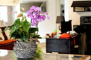 A wicker pot with purple flowers on a table in a room with a sofa and a lamp in the background. - La Villa Desenzano (Desenzano del Garda)