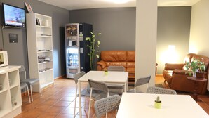 Ein Wohnzimmer mit einem weißen Tisch, grauen Stühlen, einem braunen Ledersofa, einem Bücherregal, einem Kühlschrank und einem Fernseher.