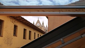 Blick durch ein Fenster eines Gebäudes mit gelber Fassade und Ziegeldach auf eine Kirche mit Spitzentürmen und einem Rosettenfenster.