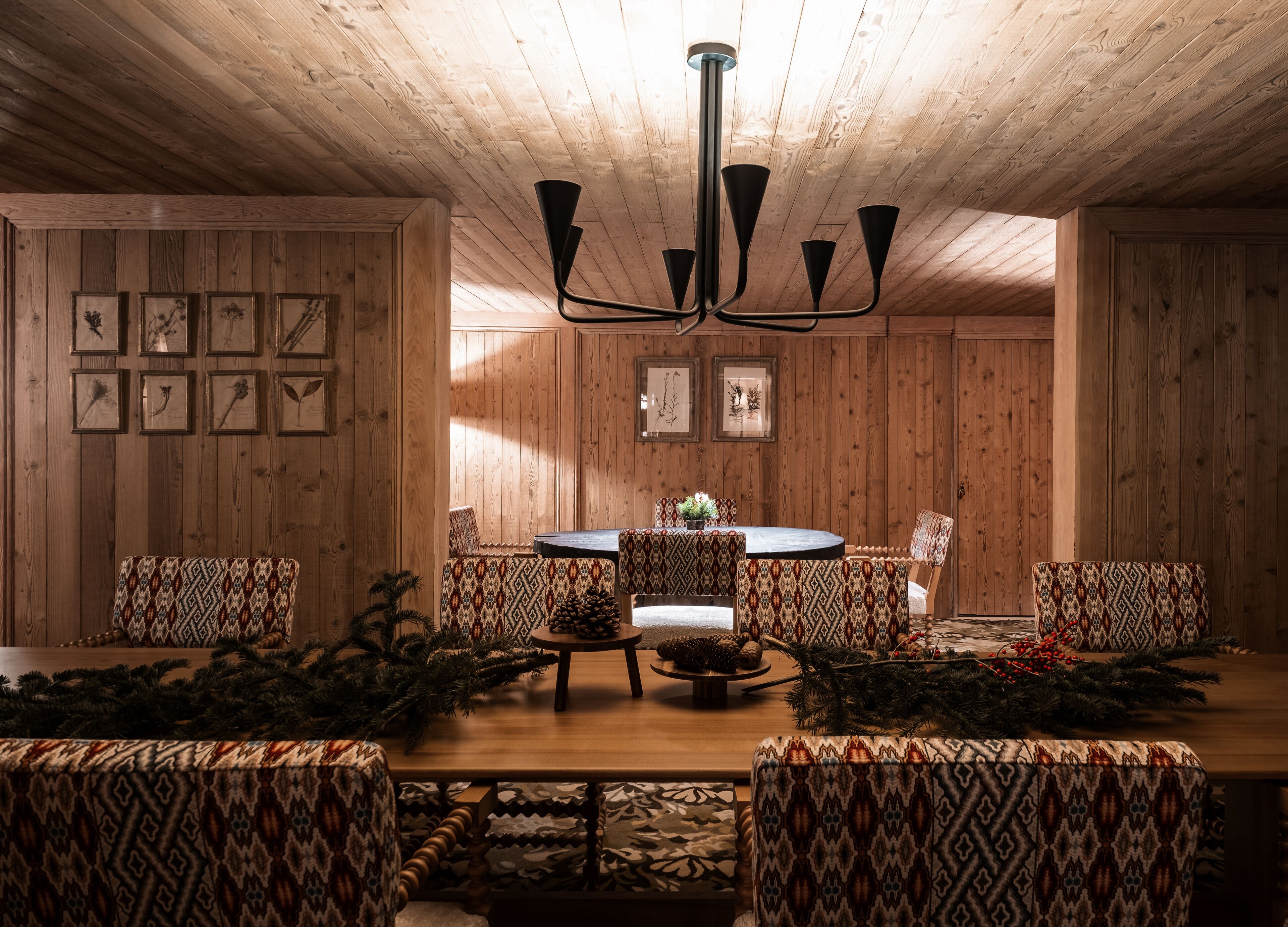 Ein Zimmer mit Holzwänden, einem runden Tisch, gemusterten Stühlen und einer Chandelüster.