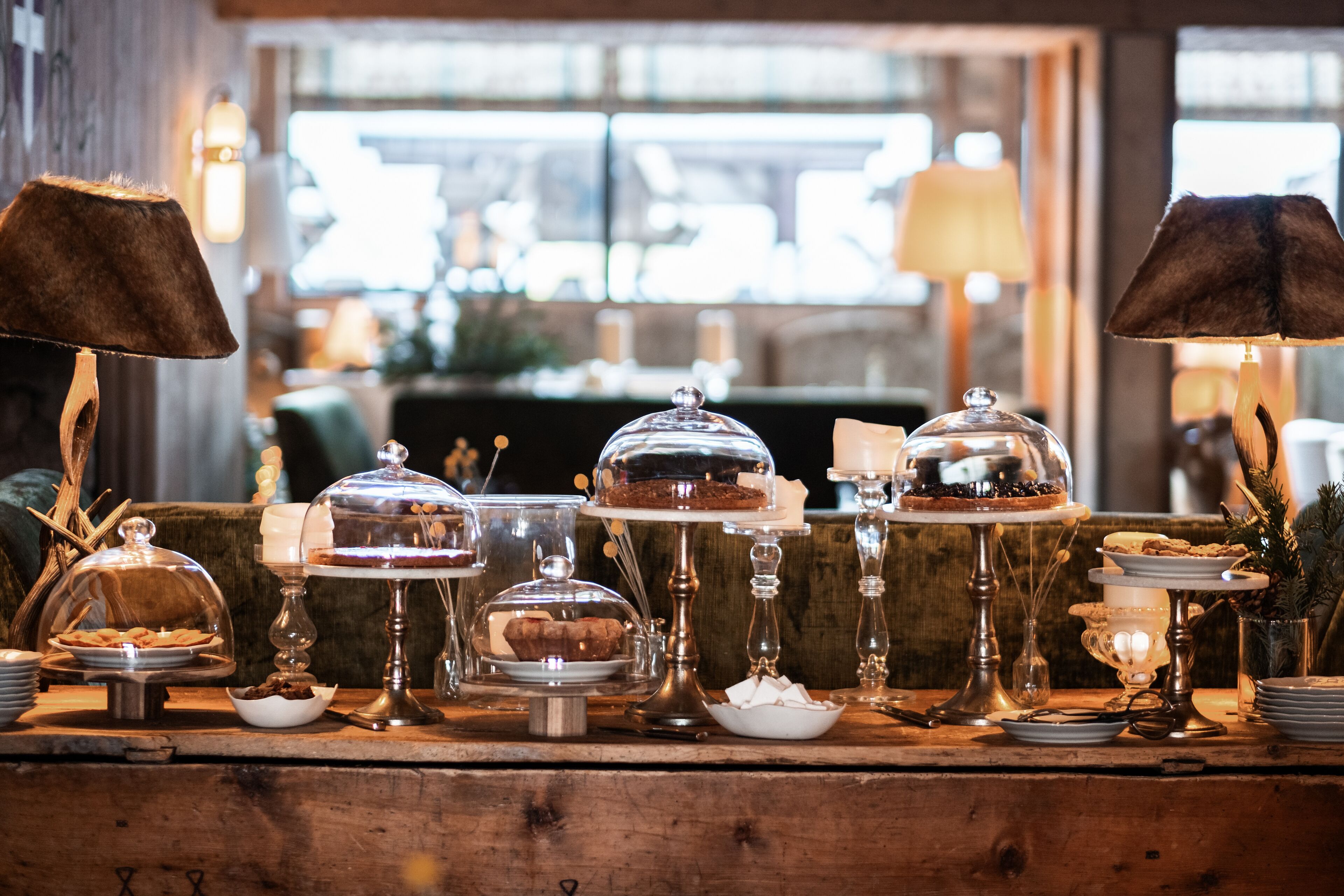 Une table de buffet présentant divers desserts sous des cloches de verre, entourée de bougies et de lampes.