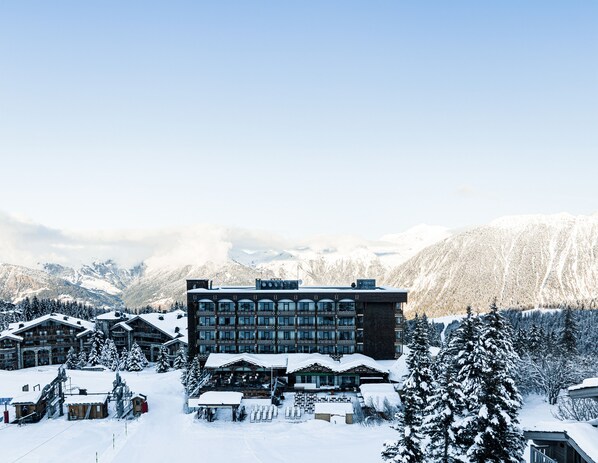 Un moderno lodge con varias construcciones, telesillas y árboles cubiertos de nieve, rodeado de montañas.