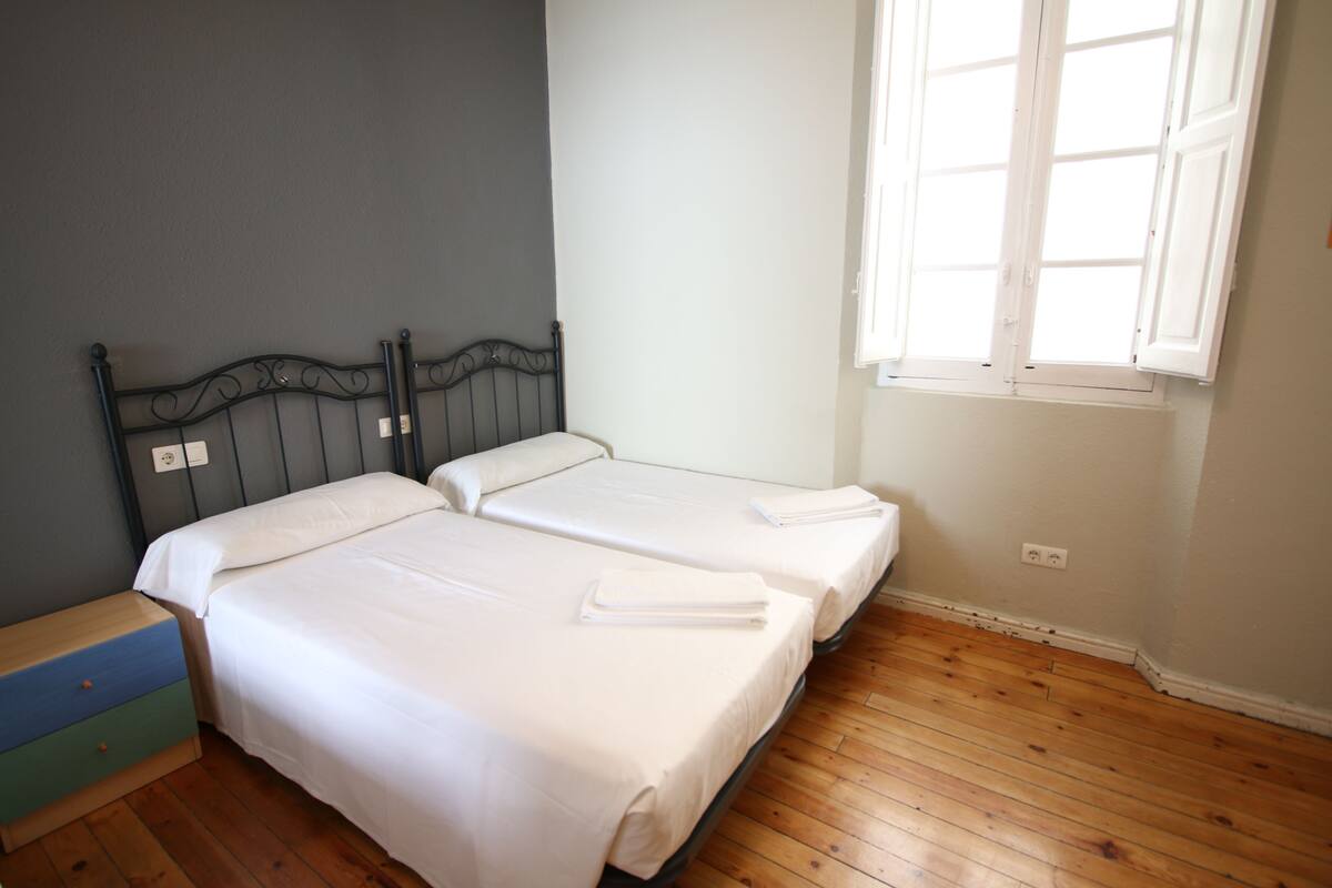 A bedroom with two beds, a wooden floor, and a window with white shutters.