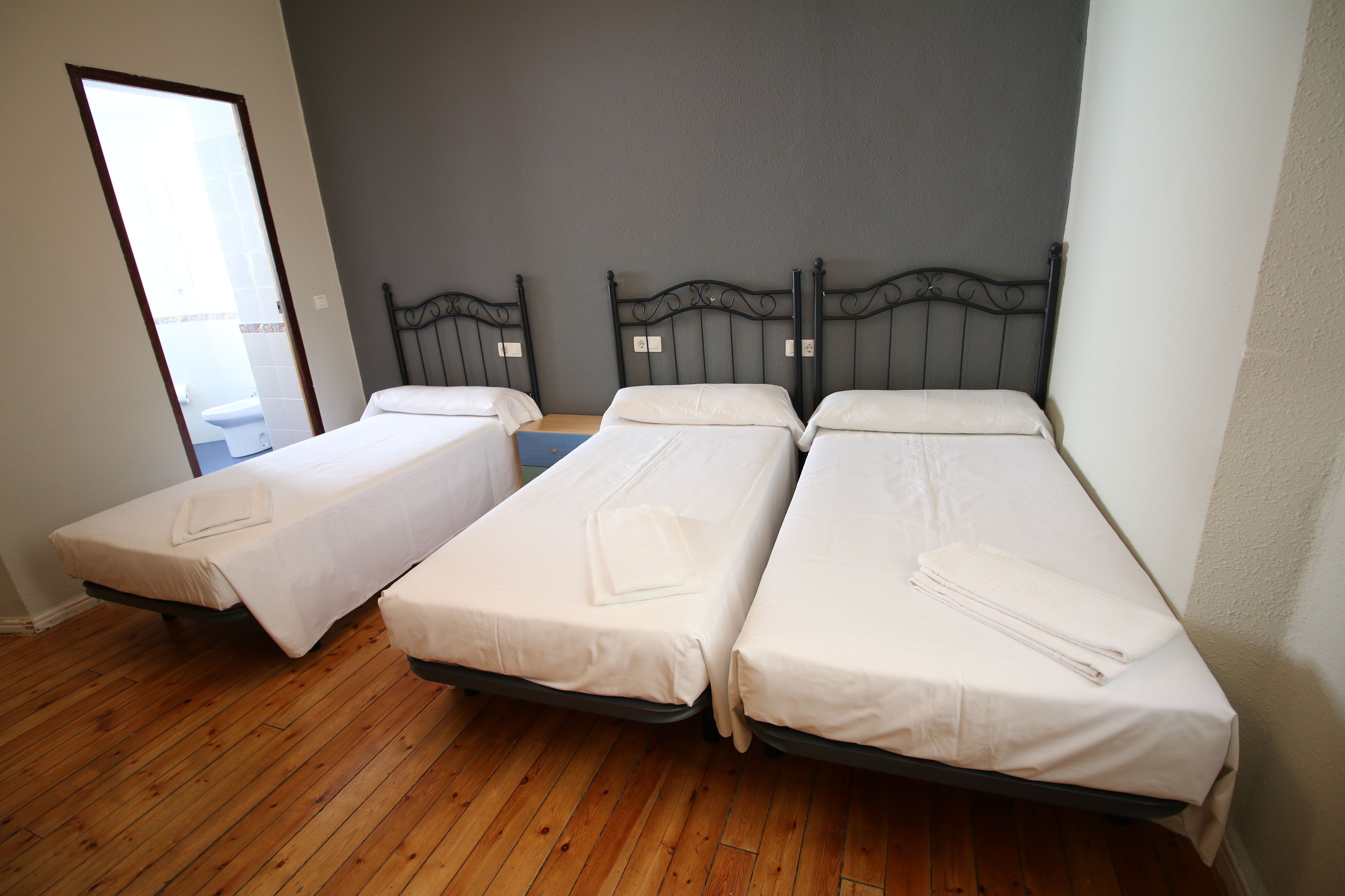 Een kamer met drie eenpersoonsbedden, houten vloeren en een grijze muur.