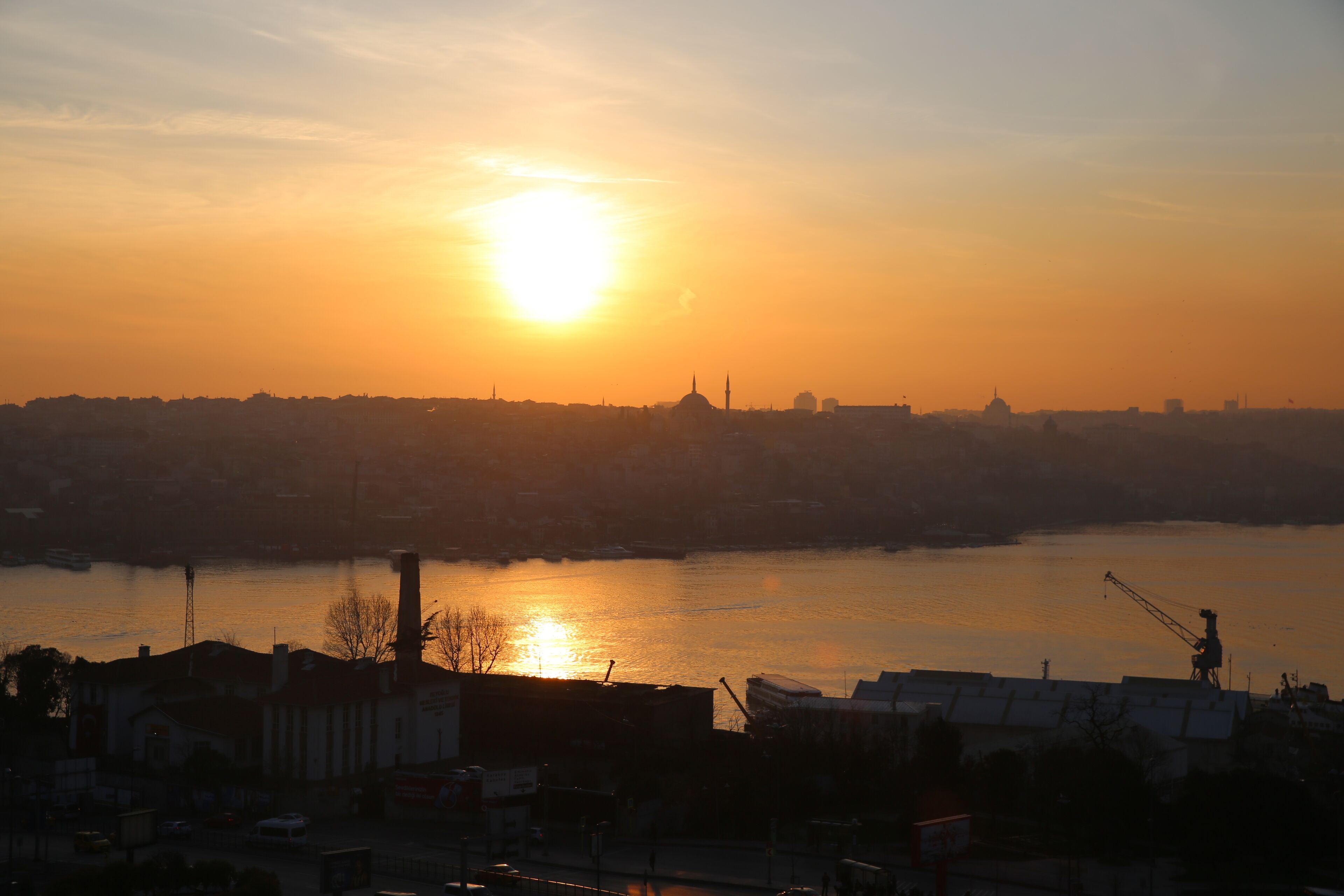 A cityscape at sunset with a river in the foreground and buildings silhouetted against the sky.